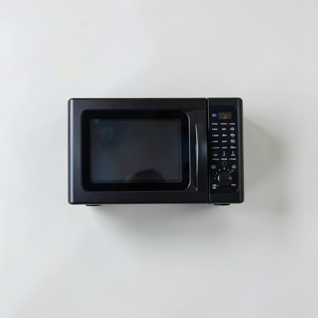 Photographie à plat d'un four à micro-ondes noir au design compact, porte fermée, posé sur une surface claire.