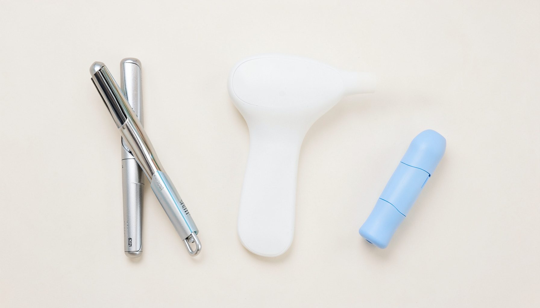 Un flat-lay épuré montrant des accessoires de soin personnel disposés harmonieusement sur une surface claire : un lisseur aux reflets métalliques, un pèse-personne au design sobre, et une tendeuse compacte. L'ambiance est douce et lumineuse, dans des tons blancs, beiges et argentés.
